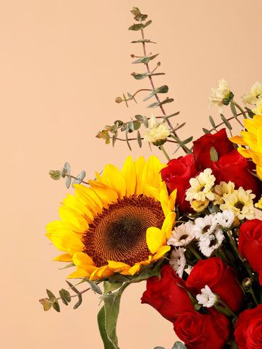 Close-up of a sunflower in a vibrant bouquet with red roses and white santnis